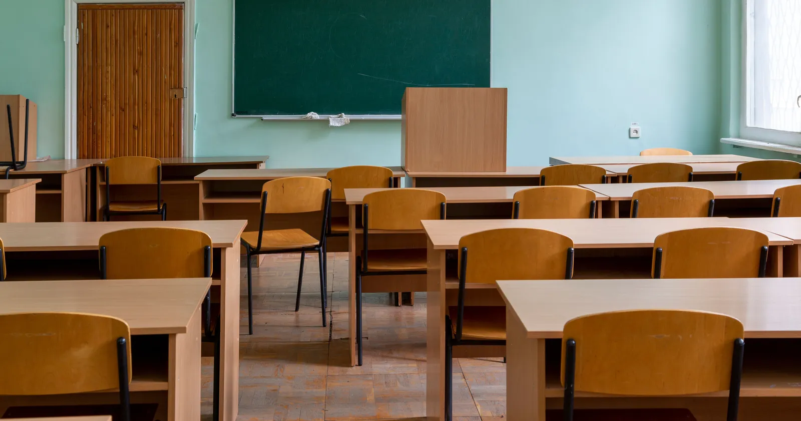 Un aula común vacía con pupitres y sillas de madera y un pizarrón verde, sin mesas de laboratorio